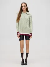 Sweater de punto color verde claro con cuello polo con cierre de cremallera, mangas largas y diseño con trenzas. Puños acanalados con rayas en color borgoña y blanco.
