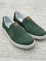 Zapato slip-on color marrón con capellada de cuero sintético microperforado, elástico lateral y suela blanca.