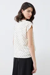 Blusa color crudo con estampado de puntos negros, de corte recto y manga corta.
