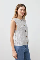 Chaleco tejido gris con botones de madera, sin mangas y cuello redondo.