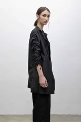 Vestido negro de microfibra con corte recto, cuello alto, cierre frontal y mangas largas con sistema de frunce ajustable.