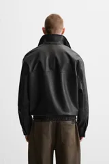 Cazadora negra relaxed fit confeccionada en tejido efecto piel. Tiene cuello solapa, manga larga con puño abotonado, bolsillos de vivo en cadera, bolsillo interior, bajo con elástico y cierre frontal de cremallera.