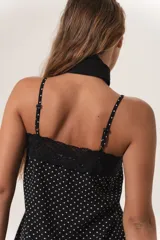 Vestido corto negro con lunares blancos, breteles finos regulables, escote recto con puntilla y terminación con puntilla. Cierre lateral invisible.