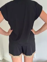 Conjunto de pijama de dos piezas color negro, compuesto por una remera de manga corta con escote en V adornado con puntilla beige, y un short con lazo frontal beige y terminación de puntilla beige en el ruedo.