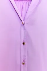 Camisa lila de satén con cuello solapa, escote en pico y manga larga. Tiene detalle de lazada en la espalda, bajo con aberturas laterales y cierre frontal con botones.
