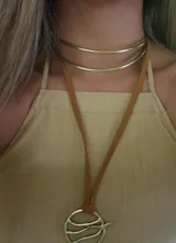 Gargantilla marrón con dije circular dorado con diseño abstracto.