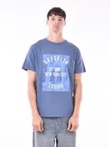 Remera azul con estampa rectangular con la palabra Brooklyn, la fecha 1998 y el puente de Brooklyn.