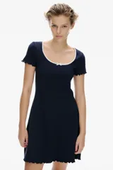 Vestido mini azul marino de manga corta en punto de algodón acanalado con pollera evasé. Modelo con cuerpo entallado y escote redondo amplio con ribete fino en color blanco y moña decorativa de satén. Ribete sobrehilado en mangas y bajo.