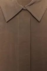 Camisa rosa de cuello solapa y manga corta con vuelta. Bajo asimétrico con aberturas laterales. Cierre frontal con botones ocultos por solapa.