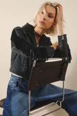 Campera corta de cuero color negro, con flecos en espalda y mangas, tachas metálicas y símil piedra cristal. Cierra con broches en el frente, tiene forrería y bolsillo interno.