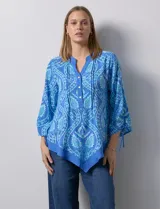 Blusa de gasa estampada marca Ruby Rd, de color azul. Tiene cuello a la base, escote en V y abertura central con botones. La delantera es plisada. Las mangas son ¾ con frunce. El ruedo y la espalda son asimétricos.
