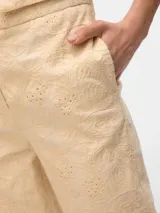 Pantalón color crema con bordado inglés, de corte tapered, tiro alto, cierre de gancho y cremallera, bolsillos delanteros inclinados y bolsillos traseros tipo ojal.