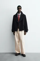 Abrigo corto azul marino de corte relajado, confeccionado en tejido con lana. Tiene cuello con solapas de pico, mangas largas con puños ajustables con trabilla, bolsillos de solapa en la cadera, bolsillo interior, abertura en el centro de la espalda y cierre frontal con botonadura.