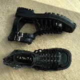 Sandalias negras de cuero vacuno con tiras entrecruzadas, suela track y cierre con hebilla en el tobillo.