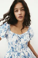 Vestido corto blanco con estampado floral azul, escote cuadrado con volados, mangas cortas abullonadas con elástico y cintura elastizada.