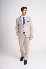 Traje de vestir color beige, compuesto por saco de dos botones con solapa de muesca, bolsillo de ojal en el pecho y bolsillos con solapa en los laterales, y pantalón de vestir de corte recto. Incluye pañuelo de bolsillo azul con lunares blancos.