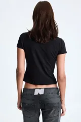 Remera negra de manga corta y corte ajustado, con estampado frontal que dice "nepo baby" en letras rojas y un corazón plateado con efecto de goteo en el centro.