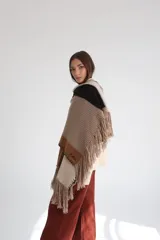 Ruana tejida con diseño geométrico en bloques de color beige, azul y naranja, con flecos en el borde inferior.