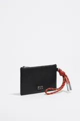 Monedero negro de piel con estructura blanda, asa de mano de cordón extraíble, logo metálico, acabados metálicos plateados, bolsillo interior y cierre con cremallera. Interior con etiqueta de tejido BIMBA Y LOLA.