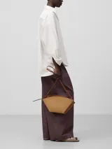 Bolso de hombro de cuero color beige y negro, con forma geométrica asimétrica y asa fina negra.