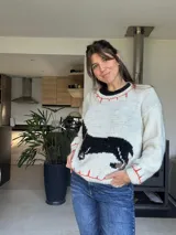 Sweater tejido color crema con cuello y puños acanalados en color naranja. Presenta un diseño bordado de un perro salchicha negro con un moño naranja.