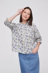 Blusa estampada con flores azules y hojas verdes, cuello mao con volados, mangas 3/4 con volados en los puños y cierre frontal con botones.