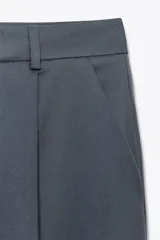 Pantalón marrón de tiro alto, corte ancho y largo midi. Presenta pinzas delanteras, bolsillos laterales y traseros de parche. Cierre frontal con cremallera y gancho metálico.