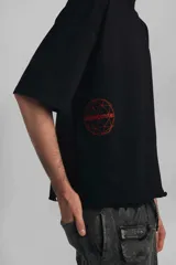Remera negra de corte amplio con mangas cortas y ruedo desflecado. Estampa circular en el frente con diseño geométrico y texto "Vancouver" en color rojo.