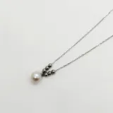 Conjunto de collar y aros en plata 925 con perlas de río. El collar tiene una cadena fina de plata con una perla central y pequeñas cuentas plateadas. Los aros son colgantes con una perla cada uno.