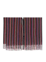 Capa tipo poncho de tejido de punto con diseño de rayas verticales en zigzag, en tonos marrones, negros, naranjas, rojos y morados. Presenta cuello en V y flecos en el ruedo.