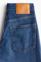 Pantalón de jean de tiro extra alto, color azul oscuro con efecto desgastado sutil. Corte de pierna amplia y recta, con puños anchos doblados. Presenta bolsillos parche cuadrados en la parte trasera y cierre expuesto en la espalda.