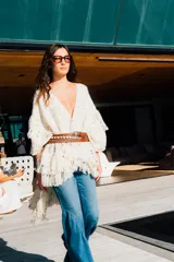 Ruana abierta color crudo tejida en lana merino con flecos largos multicolores y detalles de motas de colores.