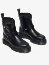 Bota biker Dr. Martens Anistone Harness, color negro, confeccionada en cuero Orleans. Presenta correas con hebillas y herrajes en plata envejecida, incluyendo una argolla metálica en el lateral. Cuenta con tirador con logo en la parte trasera y suela Bex ligeramente elevada.