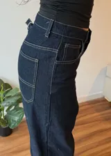 Pantalón de jean azul oscuro de corte ancho con dobladillo en color gris claro.