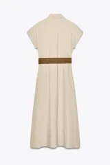 Vestido midi camisero color beige, confeccionado en lino. Presenta cuello solapa, mangas cortas con vuelta, jaretas delanteras, bolsillos laterales ocultos en costura, cierre frontal con botones y cinturón trenzado marrón.