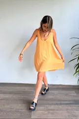 Vestido corto color amarillo mostaza, con escote en V y tirantes finos con detalle de volado o fruncido. El ruedo es asimétrico.