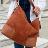 Bolso tipo hobo o tote de eco cuero con textura símil gamuza en color negro. Presenta detalles de pespuntes en color blanco en la base, que es de cuero liso negro. Tiene correa de hombro delgada y ajustable.