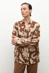 Camisa de manga larga con cuello y botones frontales, confeccionada en tela ligera con estampado floral en tonos marrón chocolate y beige claro.