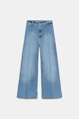 Jeans de tiro alto, pierna ancha y largo al tobillo, en denim celeste claro con efecto lavado. Presenta costura marcada en el centro de cada pierna y cierre frontal con cremallera y botón.