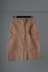 Bermuda de cuero color marrón claro, con largo por encima de la rodilla y diseño de bolsillos intervenidos mediante cortes.