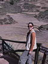 Chaleco color crema con cuello y borde de cuero marrón, con cierre de botones y bolsillos frontales.