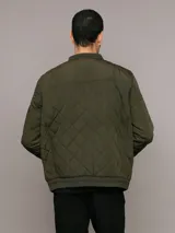 Campera bomber Calvin Klein color verde militar con diseño acolchado en forma de rombos. Tiene cierre frontal con cremallera, cuello, puños y dobladillo acanalados, bolsillos laterales y un bolsillo con cremallera en la manga izquierda con el logo de la marca.