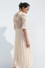 Vestido midi color crudo, con cuello redondo y mangas tres cuartos con elástico. Presenta combinación de tejidos y bordados a tono.