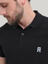 Chomba negra de algodón orgánico con cuello clásico, cartera de dos botones y logo de monograma TH bordado en blanco en el pecho.