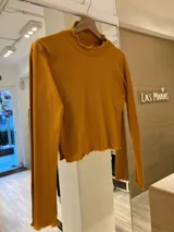 Remera gris de morley de algodón, de manga larga, con terminaciones fruncidas en cuello y mangas.