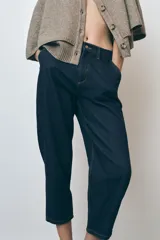 Pantalón de jean azul oscuro, corte carrot, tiro medio, largo cropped, con cintura elástica en la parte trasera, bolsillos delanteros y traseros, cierre con cremallera y botón.