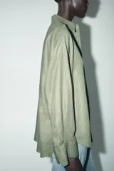 Camisa amplia color negro confeccionada con hilatura de lino. Tiene cuello solapa, manga larga, bolsillo de plastrón en el delantero, bajo asimétrico y cierre frontal con botones.