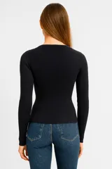 Remera negra de tejido de punto acanalado, con escote redondo con abertura en forma de gota y mangas largas. Cierre frontal con botones.