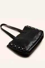 Bolso tote de cuero color marrón con tachas plateadas en los laterales. Tiene doble asa de hombro y un sobre interior de cuero.