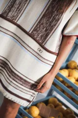 Vestido corto tejido color crudo con rayas verticales marrones y celestes. Tiene cuello redondo y mangas cortas con terminaciones en color rojo.